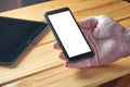 A young adult man`s hand holding black mobile phone with white empty screen on rustic wooden table. Technology, communications, Royalty Free Stock Photo