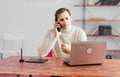 Young adult man talking on a mobile phone in the office and working on a laptop Royalty Free Stock Photo