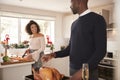 Young adult mixed race couple preparing Christmas dinner together at home, man basting roast turkey in the foreground turning to t Royalty Free Stock Photo