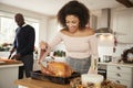 Young adult mixed race couple preparing Christmas dinner together at home, woman basting roast turkey in the foreground, front vie Royalty Free Stock Photo