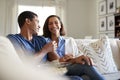 Young adult African American  couple sitting on the sofa in their living room laughing and eating popcorn, selective focus Royalty Free Stock Photo