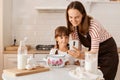 Young adult mother baking together with her daughter, sitting at table in the kitchen and finding recipe in the internet via