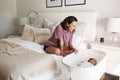 Young adult mother sitting on her bed looking down at her three month old baby sleeping in his cot Royalty Free Stock Photo