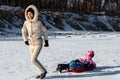 Young adult mother wear warm jacket enjoy have fun sledging two cute little sibling kids boy girl at frozen white snow Royalty Free Stock Photo