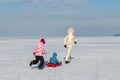 Young adult mother wear warm jacket enjoy have fun sledging two cute little sibling kids boy girl at frozen white snow Royalty Free Stock Photo