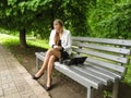 Young adult nice girl in glasses wipes her mobile by cloth, sitting on a bench with a laptop and coffee. Businesswoman in a suit