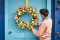 young adult placing a handmade easter wreath on a brightly painted door