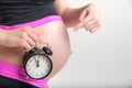 Young adult pregnant girl in sportswear with alarm clock. Time for sports concept. Yoga and fitness in anticipation of childbirth