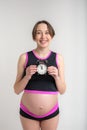 Young adult pregnant girl in sportswear with alarm clock. Time for sports concept. Yoga and fitness in anticipation of childbirth