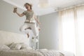 Young adult pretty woman go crazy for happiness and jump on the bed with coffee cup - overjoyed female caucasian people alone at