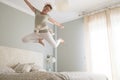 Young adult pretty woman go crazy for happiness and jump on the bed with coffee cup - overjoyed female caucasian people alone at
