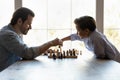 Young adult single dad playing chess with preteen son