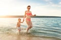 Young adult slim sporty mother enjoy having fun running water by lake or sea sand breach with cute little Royalty Free Stock Photo
