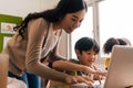 Young adult smiling beautiful Asian teacher helping elementary student boy with laptop in computer classroom Royalty Free Stock Photo