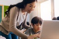 Young adult smiling beautiful Asian teacher helping elementary student boy with laptop in computer classroom Royalty Free Stock Photo