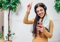 Young adult smiling cheerful girl woman listening to music from smartphone wearing wireless headset headphones and dancing while Royalty Free Stock Photo
