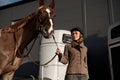 Young adult smiling rider woman stroking horse nose