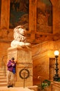 A young adult texts while standing under a statue of a lion