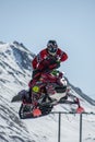 Young adult in a winter sports getup, executing a trick on a snowmobile while soaring in the air