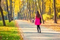 Young adult woman in bright casual coat walking along beautiful golden colored autumn park alley. Happy attractive sporty girl in Royalty Free Stock Photo