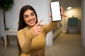 Young adult woman holding showing smartphone mock-up empty blank white screen for marketing showing close to camera and pointing Royalty Free Stock Photo