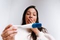 Young adult woman looking at pregnancy test with happy expression in her bedroom. latina woman with dark hair in her thirties Royalty Free Stock Photo