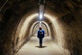 A young adult woman standing in front of an empty pathway inside Gric Tunnel in Zagreb, Croatia, illuminated by fluorescent lamps