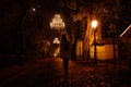 A young adult woman standing in front of an empty pathway in Zagreb, Croatia, illuminated by incandescent lamps and covered by