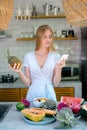 Young adult woman standing on kitchen, using smartphone