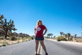 Young adult woman stands in the middle of a lone desert highway in Joshua Tree National Park