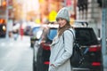 Young adult woman walking on city street wearing hat and jacket with backpack Royalty Free Stock Photo