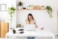 Young adult woman working on laptop computer sitting on desk at home office. Royalty Free Stock Photo