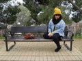 Young adult woman with yellow woolen cap sitting on a park bench thoughtful Royalty Free Stock Photo