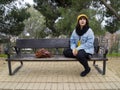 Young adult woman with yellow woolen cap sitting on a park bench thoughtful Royalty Free Stock Photo