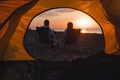 young adults couple looking on sunrise drinking coffee sitting in camping chair
