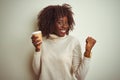 Young african afro woman holding cup of coffee standing over isolated white background screaming proud and celebrating victory and Royalty Free Stock Photo