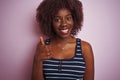 Young african afro woman wearing striped t-shirt standing over isolated pink background doing happy thumbs up gesture with hand Royalty Free Stock Photo
