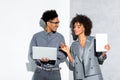 Young african amercian businessman with laptop and businesswoman with tablet in hand on grey and white