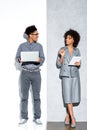 Young african amercian businessman with laptop and businesswoman with tablet in hands looking at each other on grey and white