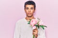 Young african amercian man holding flowers thinking attitude and sober expression looking self confident