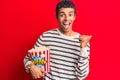 Young african amercian man holding popcorn pointing thumb up to the side smiling happy with open mouth Royalty Free Stock Photo