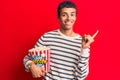 Young african amercian man holding popcorn smiling happy pointing with hand and finger to the side Royalty Free Stock Photo