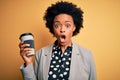 Young African American afro businesswoman with curly hair drinking cup of coffee scared in shock with a surprise face, afraid and Royalty Free Stock Photo