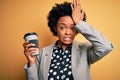 Young African American afro businesswoman with curly hair drinking cup of coffee stressed with hand on head, shocked with shame Royalty Free Stock Photo