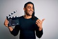 Young african american afro director man making movie using clapboard pointing and showing with thumb up to the side with happy