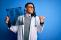 Young african american afro doctor man with dreadlocks holding chest lung xray pointing and showing with thumb up to the side with Royalty Free Stock Photo