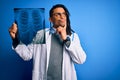 Young african american afro doctor man with dreadlocks holding chest lung xray serious face thinking about question, very confused