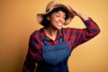 Young African American afro farmer woman with curly hair wearing apron and hat very happy and smiling looking far away with hand Royalty Free Stock Photo