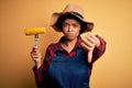 Young African American afro farmer woman with curly hair wearing apron holding cob corn with angry face, negative sign showing Royalty Free Stock Photo