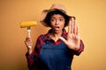 Young African American afro farmer woman with curly hair wearing apron holding cob corn with open hand doing stop sign with Royalty Free Stock Photo